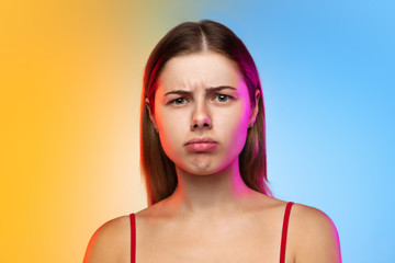 Thoughtful. Close up caucasian young woman's portrait on gradient studio background in neon. Beautiful female model in casual style. Concept of human emotions, facial expression, youth, sales, ad.