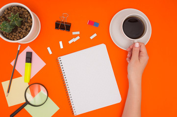 The concept of working in the office, relaxing while working, coffee break, mockup in an empty notebook. Hand holding a Cup of coffee. Office supplies, cactus in a pot. Top view, color background.