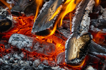 Burning oak wood in Russian stove. Stove in country house. Bright flame over hot coals. Close-up. Embers glow against blurred orange flame background. Selective focus.
