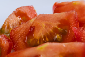 Stücke von geschnittenen saftig roten Tomaten vor weißem Hintergrund, fertig für die Zubereitung