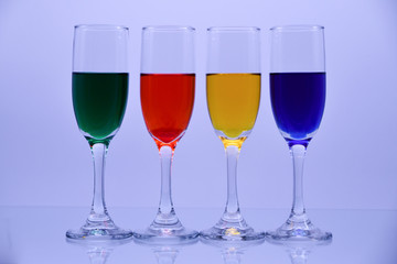 Flute glasses filled with green, red, yellow and blue liquid colors.
