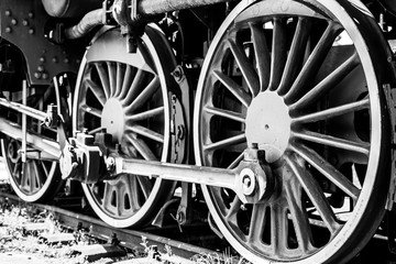 Huge vintage steam locomotive, red painted steel wheel detail close up. Coal-powered steam train stands on a siding. Classic gigantic heavy railway machinery. Side view of power parts of machine.