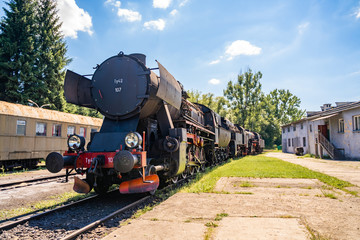 Huge vintage steam locomotive, red painted steel wheel detail close up. Coal-powered steam train stands on a siding. Classic gigantic heavy railway machinery. Side view of power parts of machine.