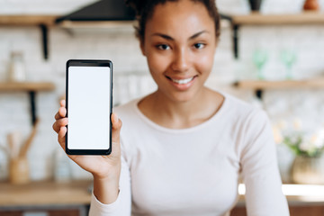 Smiling, beautiful girl sitting in the kitchen, holding a phone in her hands with copy space