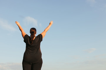 Fototapeta na wymiar Body positive, freedom, high self esteem, confidence, happiness, inspiration, success, positive affirmation. Overweight woman celebrating rising hands to the sky
