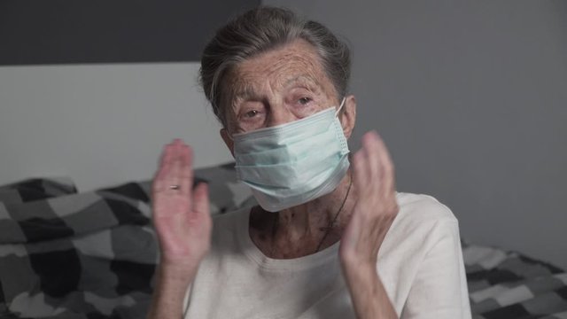 Very old grandmother is quarantining at home. Pensioner puts on protective mask in bedroom. Senior woman with medical mask at the home during coronavirus, covid-2019 pandemic, stay home