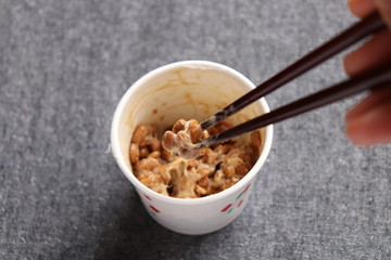 Natto, fermented soybeans in paper cup and close-up of sticky soybeans taken by chopstics