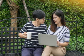 LGBT and bisexual concept.Lesbian couples so happiness with girlfriend drinking coffee and check E mail together with laptop at park in the morning. 