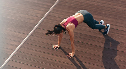 Top full lenght view of a sporty woman in push up position doing exercises outdoors. Athlete girl doing fitness training with her hands on the floor outside on a sunny day.