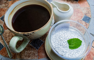 A large Cup of coffee, Chia pudding on coconut milk with a mint leaf and cream in a milk jug on the table