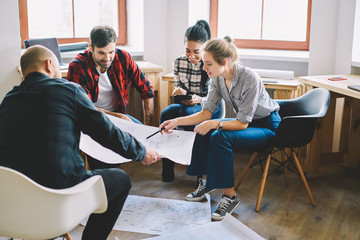Skilled male coach checking architectural projects of young students brainstorming working in...