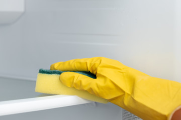 Hand of a woman in yellow glove cleaning the fridge shelf