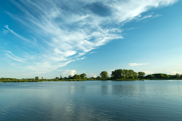 White clouds blowing in the blue sky over a peaceful lake