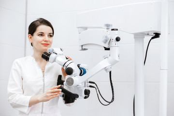 A beautiful and cute dentist in a white coat holds medical equipment in his hands and looks to the side.