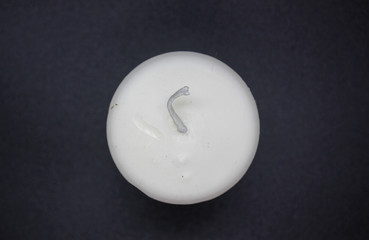 Top view of a white wax candle on a black background. White unlit round candle