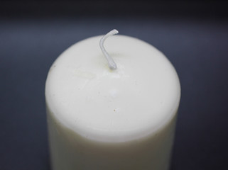 A white unlit candle on black background. Wax white candle