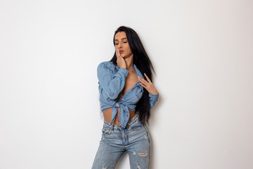 Beautiful sexy young woman in jeans stranding in front of white wall and posing