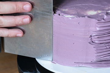 Confectioner using bench scraper to finish the cake.