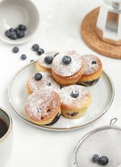 Muffins on a gray plate on a light table with a cup of coffee, blueberries and a coffee pot