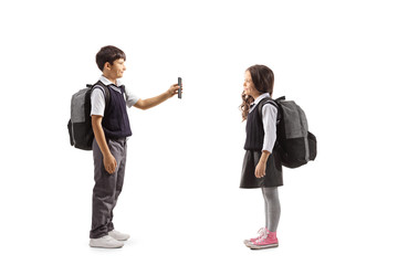 Schoolboy in a uniform standing and showing a smartphone to a schoolgirl