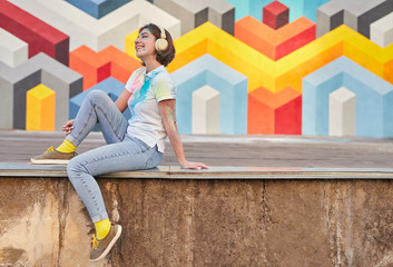 Optimistic woman listening to music near graffiti wall