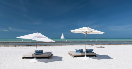 Fototapeta na wymiar Panoramic view of a Caribbean beach a few meters from the Mexican Caribbean Ocean. Umbrellas and sunbeds on the beach. In the background, a catamaran sails off the coast of Holbox Island, Mexico