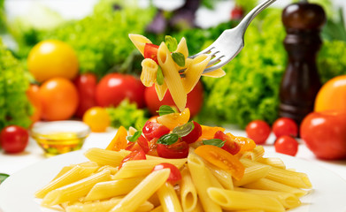 Plate of italian pasta, penne rigate on fork with tomatoes and basil