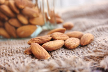 close up roasted organic brown almond seed  on sack floor  and  some of almond in the  square bottle.