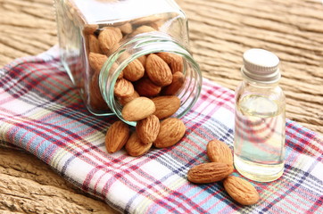 roasted organic brown almond seed on plaid  and  some of almond in the square bottle with almond oil in the bottle.