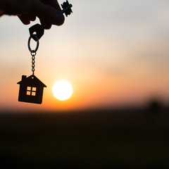 Silhouette of a house figure with a key, a pen with a keychain on the background of the sunset. They dream of a house, building, moving to a new house, mortgages, renting and buying real estate. Copy 