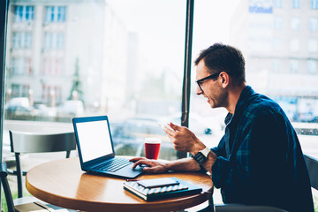 Naklejka premium Good looking smiling professional male freelancer in trendy eyewear watching funny video in popular webpage using laptop computer with blank screen connected to 4G internet while sitting indoors
