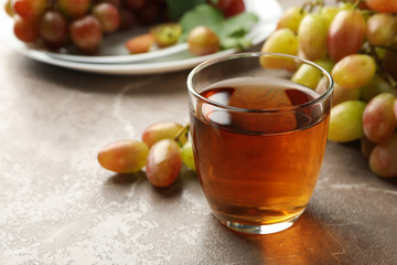 Glass of juice and plate with grape on gray background