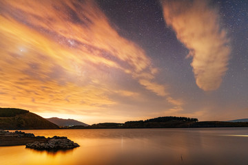 Beautiful night landscape, starry sky with bright clouds and  milky way galaxy above the lake. Astronomical background.