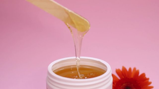 Sugar paste in a white jar on a pink background.A master in pink gloves stir the sugar paste before removing unwanted hair.Sugaring.Depilation. Epilation.Beauty concept.Selective focus on sugar paste.