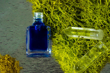 A bottle of aurasoma with the blue essence and crystal on the moss background.