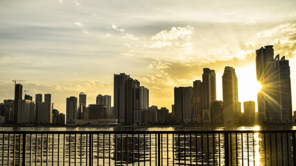 Sharjah skyline with the sun setting between the buildings. The picture was taken from the railing by Khalid Lake.