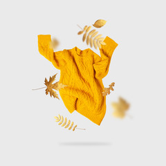 Yellow orange flying women's knitted sweater and golden autumn leaves on light gray background....