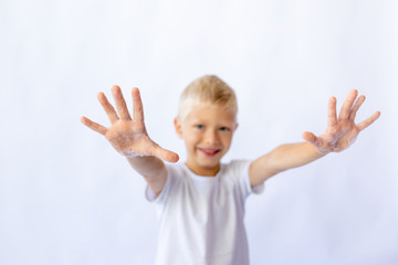 child boy in a white t-shirt shows hands in foam on a white isolated background, hands in focus. World hand washing day