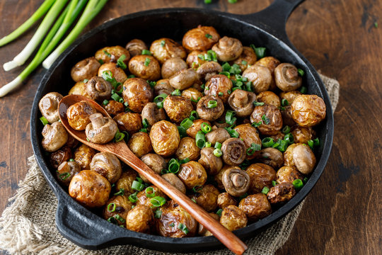 Delicious baked potatoes in cast-iron pan with champignons and green onion. Dish for dinner
