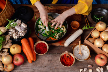 Asian women wearing Korean traditional costumes (hanbok) are mixing fresh stir-fry and kimchi ingredients with ingredients such as salt, garlic, gochugaru, fresh vegetables.