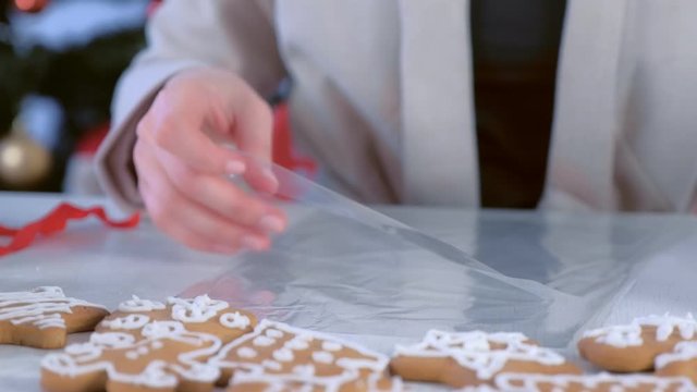 Woman packaging gingerbread man cookies with icing for Christmas sitting at table, hands closeup. Preparing presents, gifts in New Year time. Homemade sweet bakery.