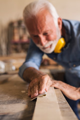 Experienced carpenter sandpapering a wooden plank