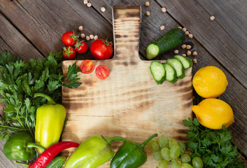 Fresh vegetables and raw ingredients for cooking around wooden cutting board on rustic table top view, place for your text