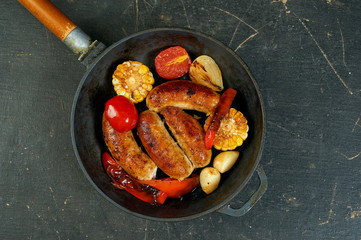 fried homemade sausages with vegetables in a pan .cooking at home