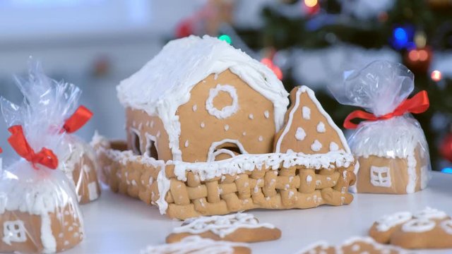 Small and big gingerbread houses and cookies in package for Christmas on table on Christmas tree background with blinking garlands. Preparing presents, gifts, New Year festive atmosphere.