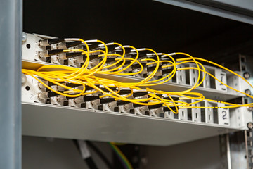 Many yellow fiber optic cables are inserted into the switches in multiple rows. Cable management. Horizontal orientation.