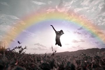 young boy jumping high in air against sunset with rainbow .