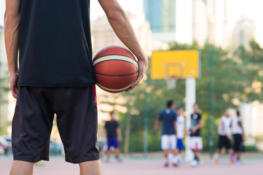 Closeup of basketball player holding a ball while watching the game on the sideline at an outdoor court in the city.