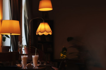 interior in a cafe with lampshades, a table with two glasses of coffee latte  in warm dark colors,...