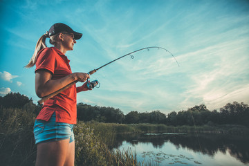 Cute caucasian woman is fishing with rod on the summer lake
